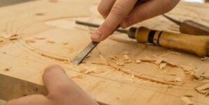 Handen bewerken een houten plank met een beitel in een werkplaats